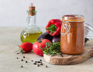 Vegetable caviar in jar, fresh eggplants, bell pepper, tomatoes and thyme on wooden board. Homemade preserves. Vegetarian cuisine. Autumn harvest.
