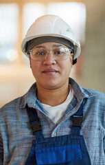 Vertical portrait of female worker wearing hardhat and looking at camera while standing on construction site