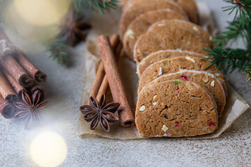 Danish spicy butter cookies with candied fruits, cinnamon sticks and anise, light background. Festive Christmas or New Year background with fir branches and garland bokeh.