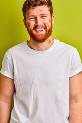 happy male with red kisses marks on cheek, enjoy. caucasian guy in white t-shirt posing isolated in studio