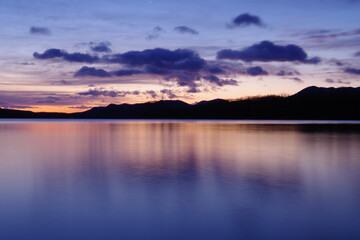 鮮やかなグラデーションの空に浮かぶ雲。湖面に映る黄昏の空が美しい明媚な風景。