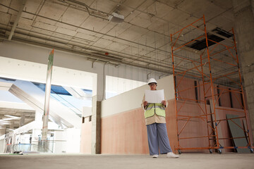 Wide angle portrait of contemporary female engineer looking at documents while standing on construction site, copy space
