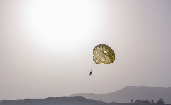 Parachute parasailing of tourists on a sandy beach Sunny weather against the background of clear sea and ocean.The wind blows up the canopy of the parachute against a clear blue sky with clouds