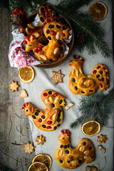 Christmas brioche buns in rooster shape decorated with dried fruits and almonds and gingerbread cookies on wooden table.