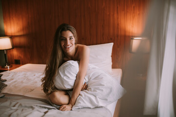 Beautiful young woman sitting on a bed in the morning