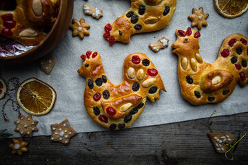 Christmas brioche buns in rooster shape decorated with dried fruits and almonds and gingerbread cookies on wooden table.