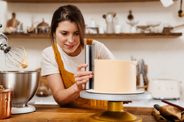 Beautiful pleased pastry chef woman making cake with cream