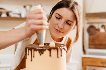 Fototapeta premium Beautiful pleased pastry chef woman making cake with chocolate cream