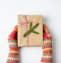 female hands in knitted mittens hold a box wrapped in brown paper and tied with a rope on a white background