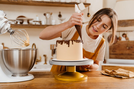 Beautiful pleased pastry chef woman making cake with chocolate cream