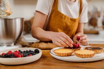 Caucasian pastry chef woman making tarts with berries at cozy kitchen