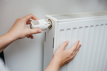 Close up shot of Caucasian female's hand adjusting radiator temperature using thermostat. Home with...