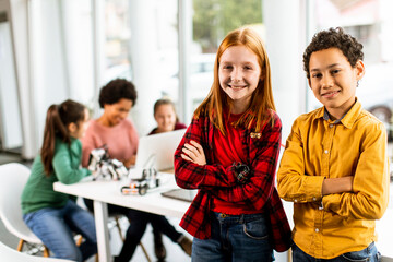 Best friends standing in front of kids programming electric toys and robots at robotics classroom