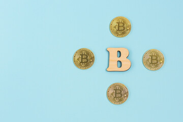 Bitcoins and next to wooden with B letter on blue background. The future of money. Copy space.