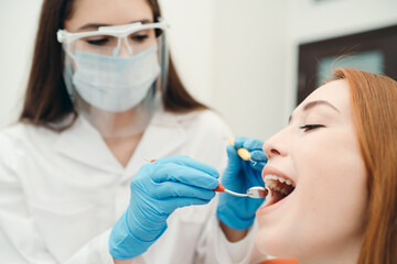 Woman in a protective mask and gloves examines the oral cavity of a Caucasian girl