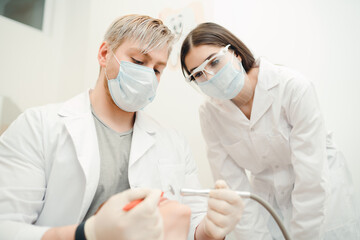 Specialists in white coats remove caries from a patient in a clinic. Healthy teeth