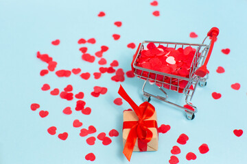 Shopping cart machine with many red hearts and little gift box near on blue background. Valentines...