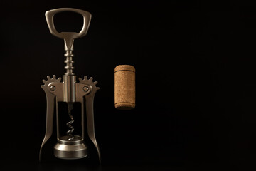 Metal corkscrew and wine cork on the black background with the copy space
