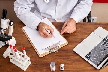 top view on cropped doctor making notes sitting at table, make research with test tubes of coronavirus, using laptop