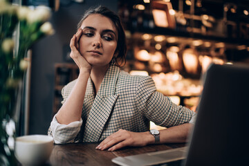 Thoughtful lady using laptop and enjoying coffee in cafe