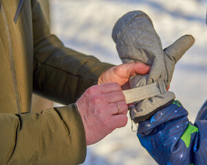 A man puts a mitten on his son's hand.