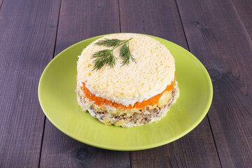 Layered round salad with vegetables and salmon Mimosa on a plate on a wooden background
