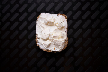 Rustic piece of bread with sour cream and cheese on a modern black background