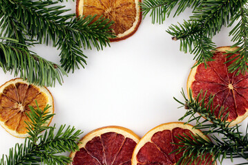 White background with green branches of a christmas tree and citrus dried fruits