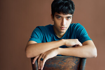 Stylish handsome young man posing on studio sitting on a chair looking to camera