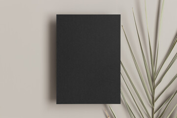 Black invitation card mockup with a palm leaf on a beige table. 5x7 ratio, similar to A6, A5.