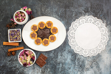 a plate of assorted cookies with different types of dry flower and a piece of lace on grey ground