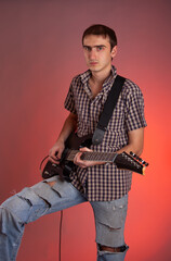 Expressive young man playing guitar on red background. Musician in beautiful hall. 