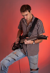 Expressive young man playing guitar on red background. Musician in beautiful hall. 
