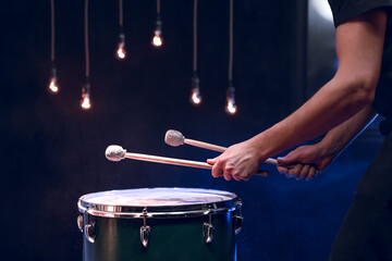 The drummer plays with mallets on floor tom in dark room.