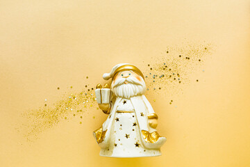 Toy Santa Claus with a gift box of gold color on a yellow background. Holiday concept, Flat lay, top view, copy space
