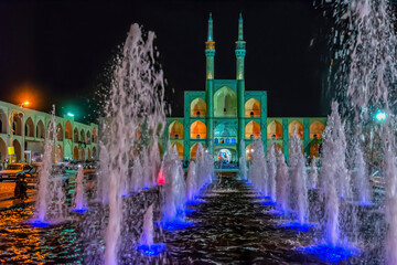 Musical color fountain with blue illumination at night. In the background is a green Chakhmaq mosque. Yazd, Iran