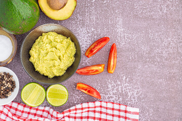 Organic avocado with seed, avocado halves, whole fruit, and fresh guacamole in a bowl with salt and pepper on a small dish on gray stone background. Top view. Concept of healthy fruit