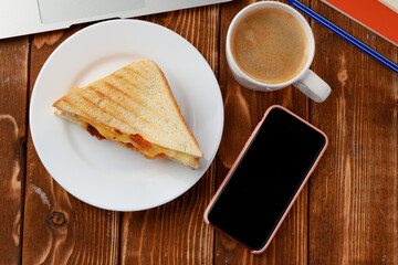 Triangle sandwich on wooden office table with laptop and coffee cup