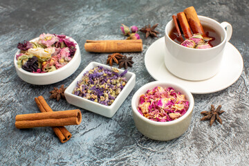 sidewise shot of herbal tea with dry flowers and cinnamon sticks on grey ground