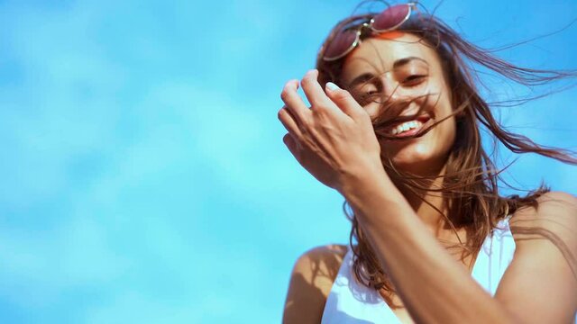 beautiful carefree smiling young woman looking down at camera on blue sky background. wind blowing hair, focus moving from face to flying hair