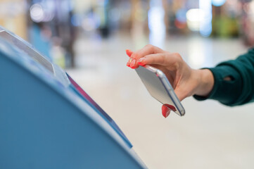 A faceless woman scans the qr code from her smartphone. A girl uses a self-service machine at the airport to check in for a flight and print tickets