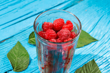 fresh raspberries in a glass glass with leaves on an old wooden background