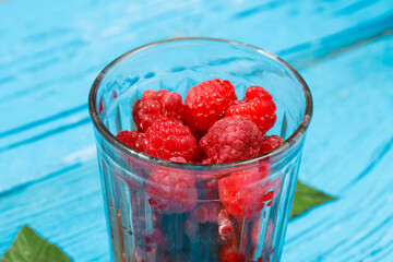 fresh raspberries in a glass glass with leaves on an old wooden background