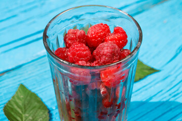 fresh raspberries in a glass glass with leaves on an old wooden background