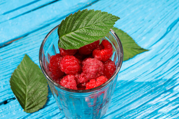 fresh raspberries in a glass glass with leaves on an old wooden background