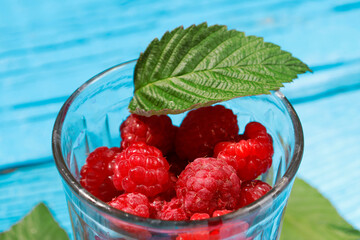 fresh raspberries in a glass glass with leaves on an old wooden background