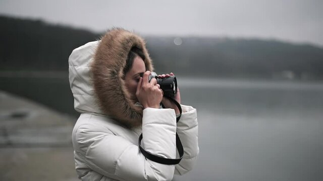 Woman in white winter coat taking photos and shooting video on a vintage camera