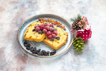 top view raisin cake slices with raisins and raspberries on blue oval plate and xmas toys on marble ground