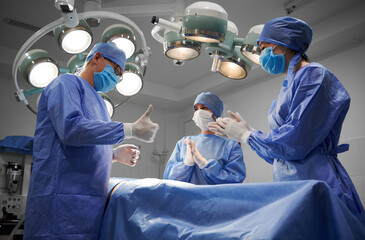 Group of doctors in sterile gloves and protective face masks standing by patient after successful...