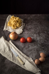 Fresh onions, eggs, tomatoes and raw pasta with knife and table cloth on a stone table